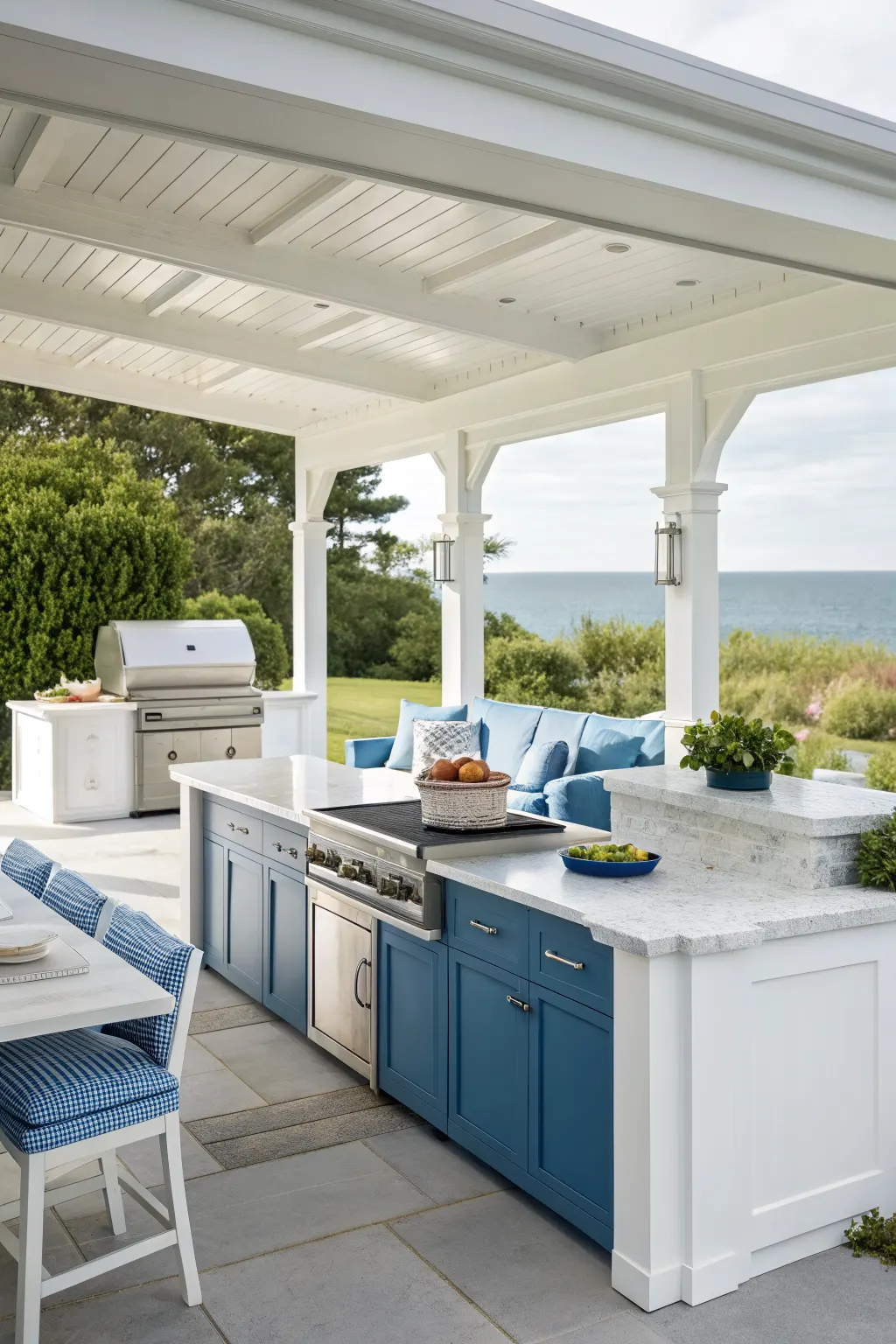 Covered patio kitchen with blue cabinets, white counters, grill, and ocean view seating area