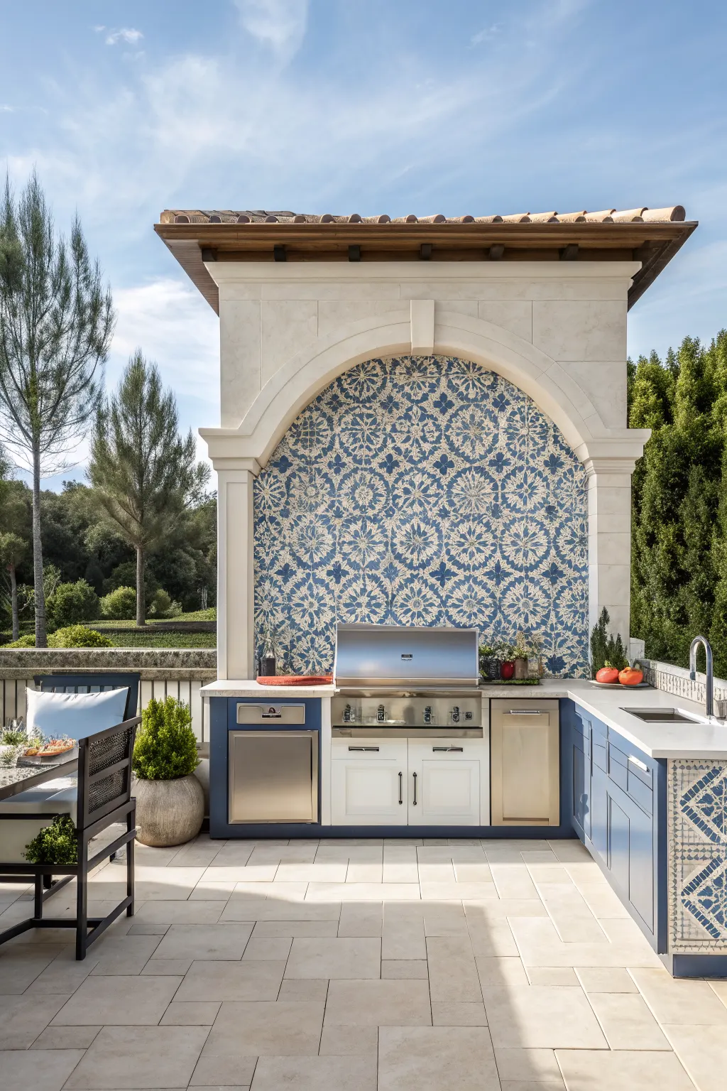 Outdoor kitchen with blue patterned tile backsplash, stone arch, grill, and blue cabinets on patio
